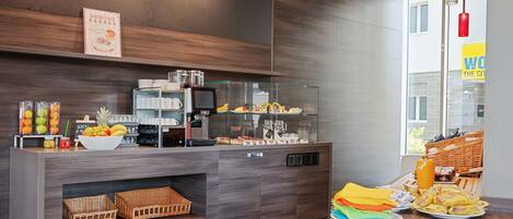 A modern breakfast bar with a coffee machine, fruit bowl, and various food items.