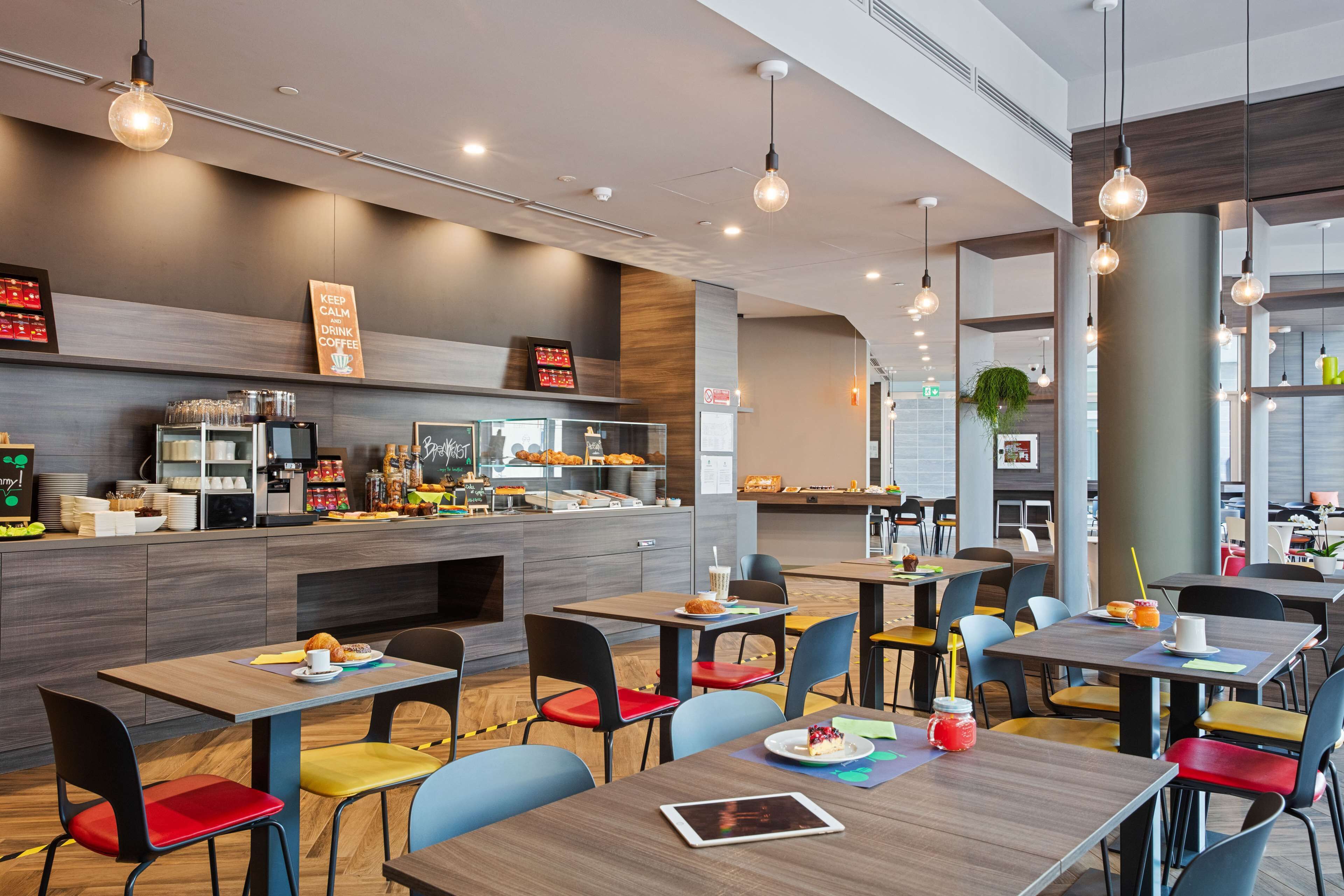 A modern cafe with multiple seating areas, a coffee bar, and a variety of food and drink options.