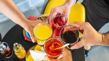 Eine Gruppe von Personen hält verschiedene Getränke, darunter ein Glas Orangensaft, ein Glas rotes Getränk und ein Glas dunkle Flüssigkeit, möglicherweise Wein oder Whiskey.