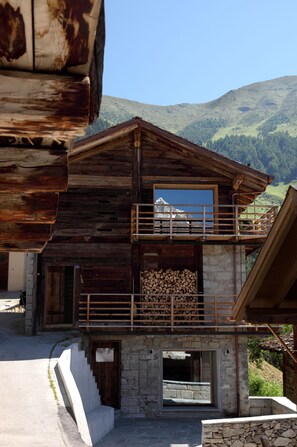 A wooden chalet with a stone base, a balcony with a metal railing, and a view of a mountain. - Montagne Alternative (Orsieres)