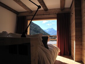 A bedroom with a bed, a window with curtains, and a view of mountains. - Montagne Alternative (Orsieres)