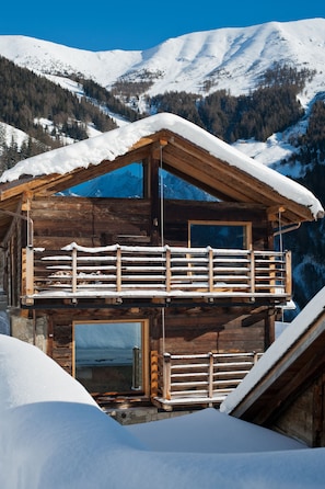 A wooden chalet with a balcony and large windows, surrounded by snow-covered mountains. - Montagne Alternative (Orsieres)