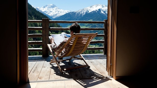Eine Holzterrasse mit einem Holzstuhl, der Blick auf ein Gebirge bietet.
