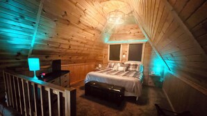 A cozy attic bedroom with a bed, bedside table, and a lamp.