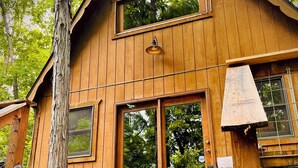 A wooden cabin with a large central window, smaller side windows, and a bell light above the door.