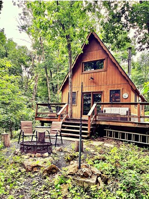 Une cabane en bois dotée d’un porche, d’un foyer et offrant une vue sur la forêt environnante.