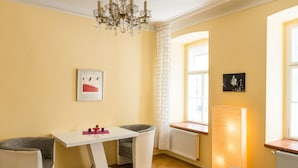 A modern living room with a white table, two grey armchairs, a chandelier, and a window with a view. - Apartment Annabelle (Vienna)