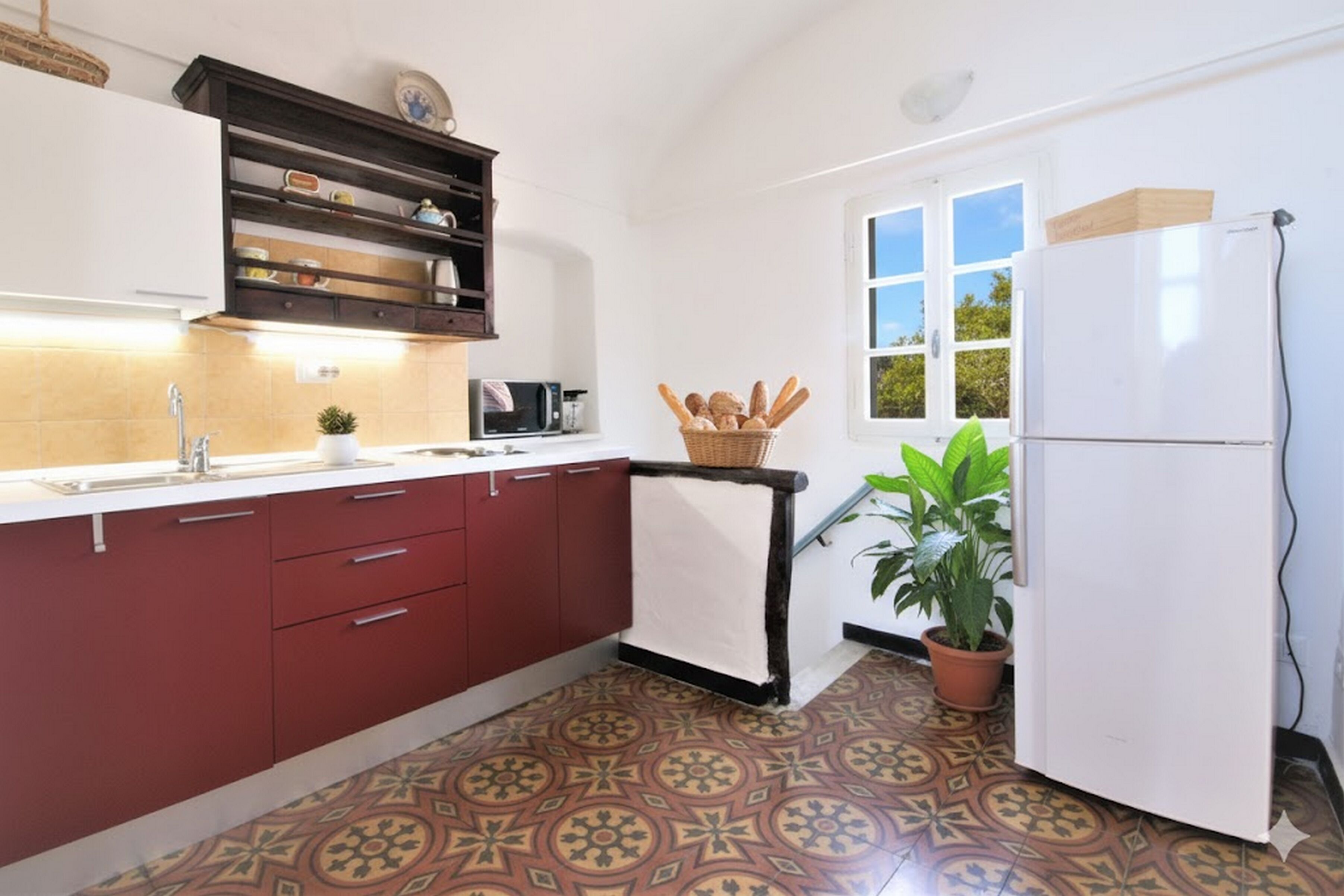 A compact kitchen with a patterned tile floor, a white refrigerator, a microwave, and a shelf with jars.