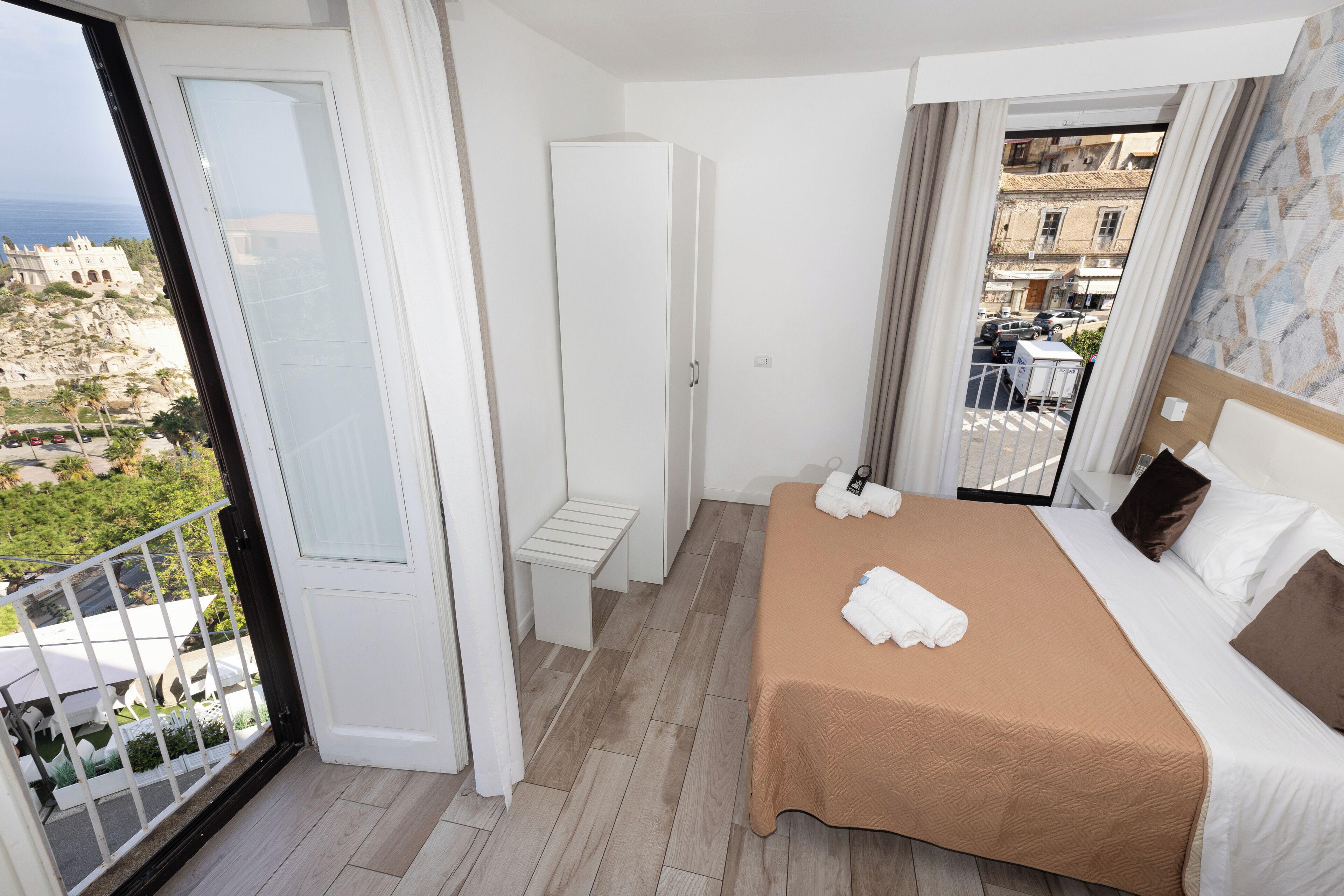 Une chambre d’hôtel comprenant un lit, un petit coin salon, une armoire et un balcon avec vue sur la ville.