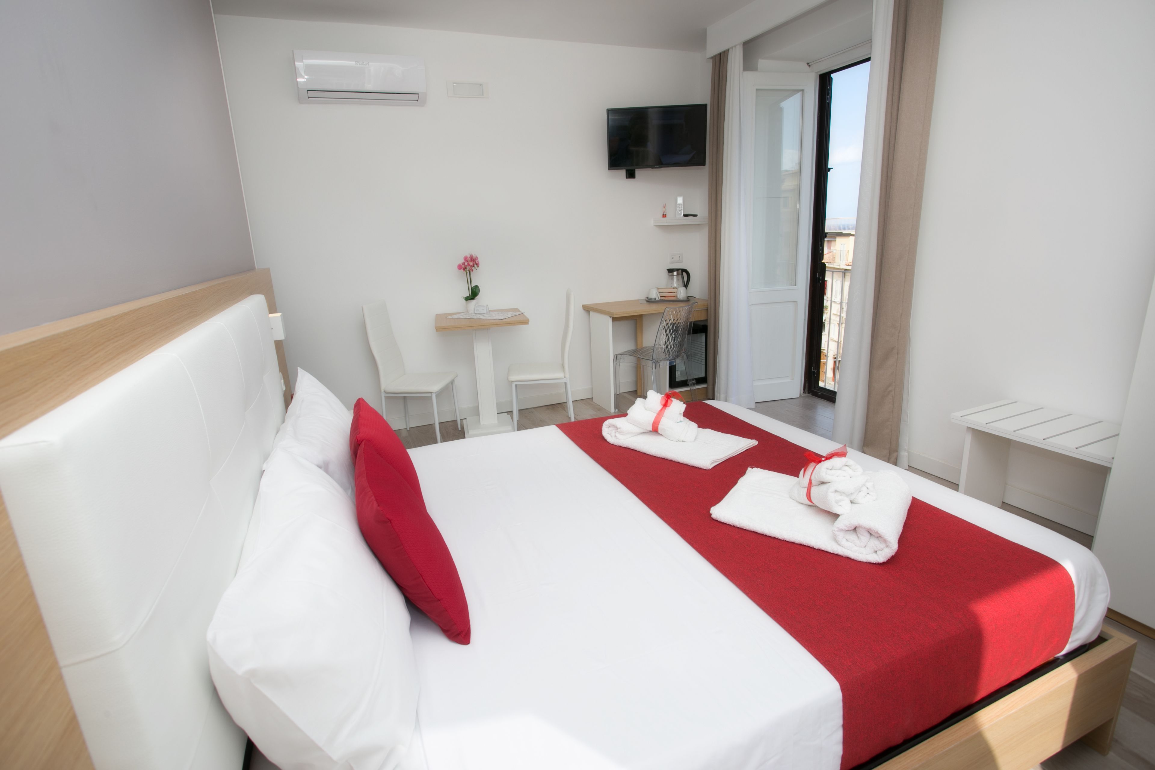 A hotel room with a bed, a desk, a chair, a TV, and a balcony.