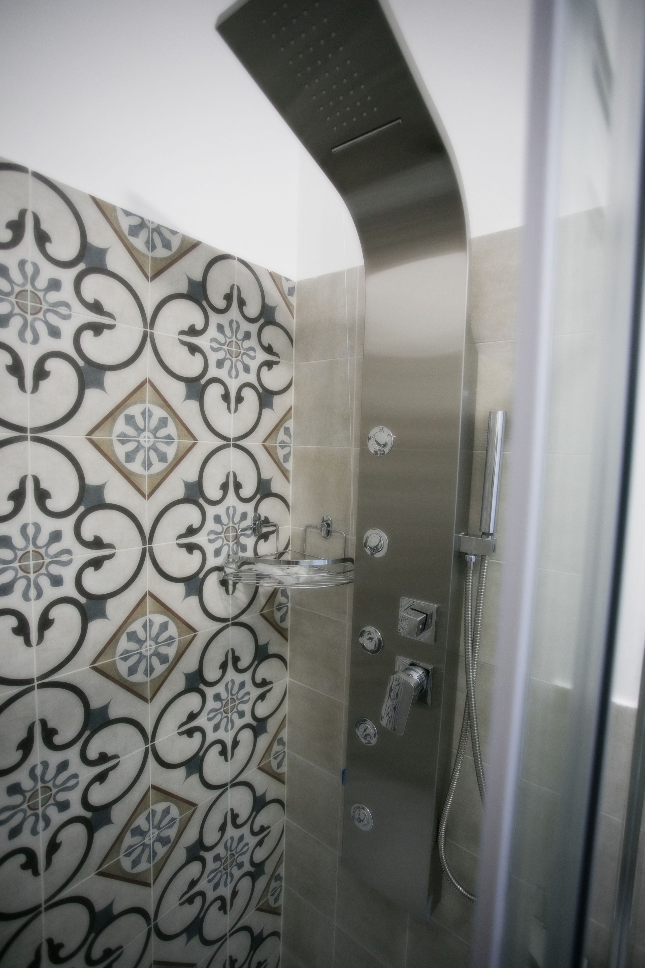 A modern shower with a glass door, a wall with decorative tiles, and a metallic showerhead.