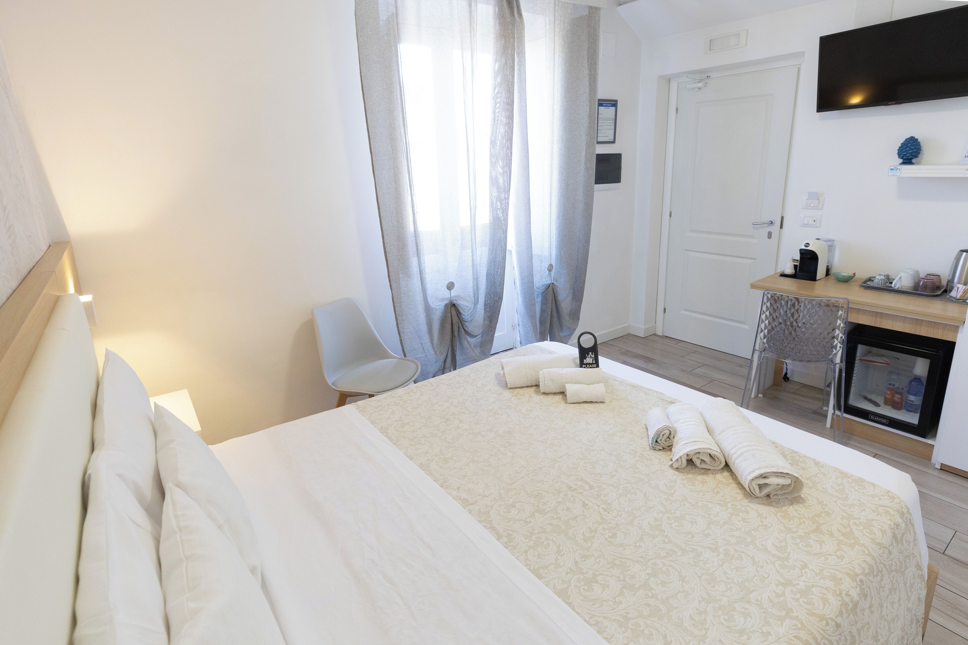 Quarto de hotel com cama, escrivaninha, cadeira e televisão.