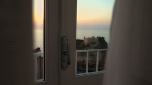 Vista desde una habitación con puerta que da a un balcón con vistas a la costa, edificios y cielo despejado.