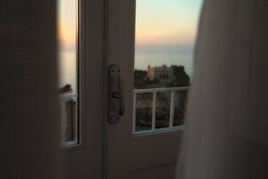 Vista desde una habitación con puerta que da a un balcón con vistas a la costa, edificios y cielo despejado.