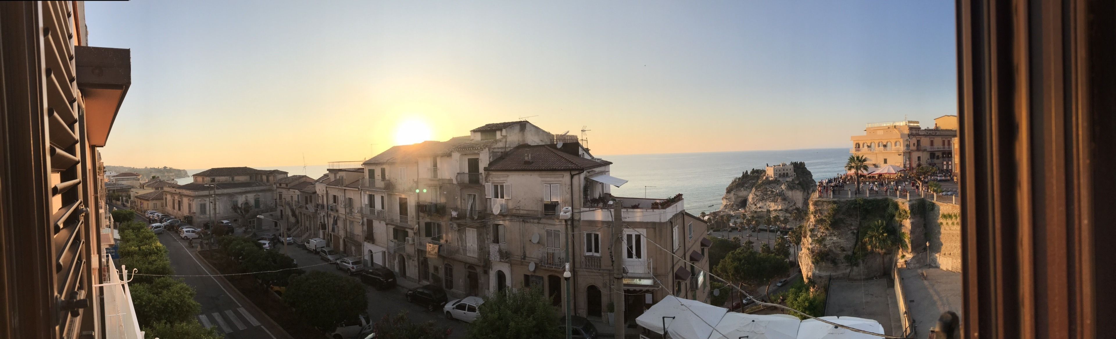 Un paisaje urbano costero con edificios que dan al mar, cielo despejado y un atardecer.