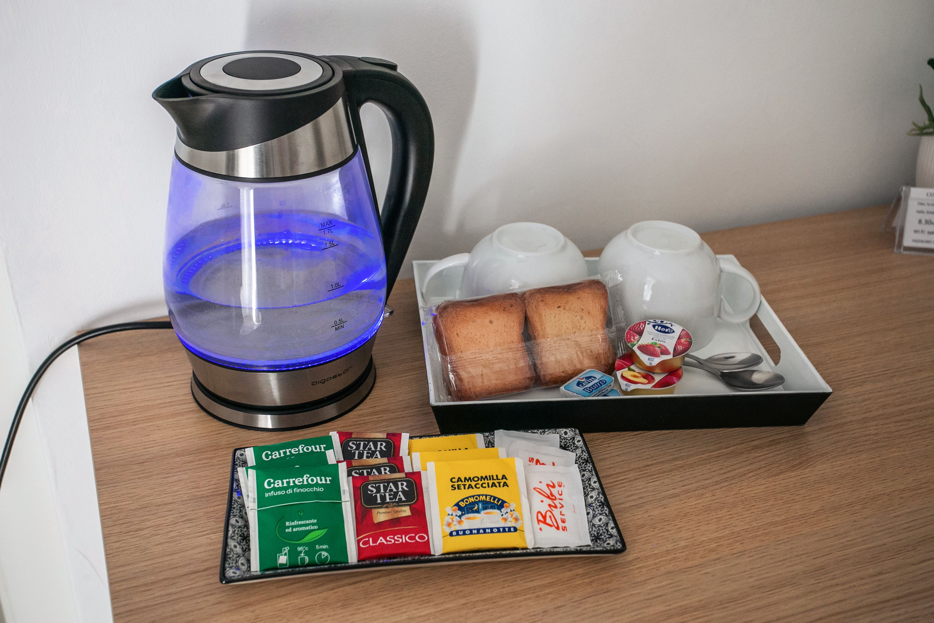 Una cafetera, una bandeja con pan y un pequeño recipiente de yogur, y una variedad de cápsulas de café sobre una mesa de madera.