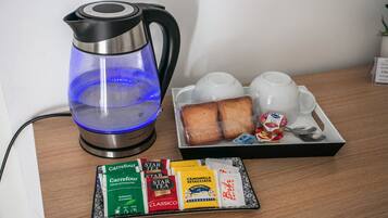 Una cafetera, una bandeja con pan y un pequeño recipiente de yogur, y una variedad de cápsulas de café sobre una mesa de madera.