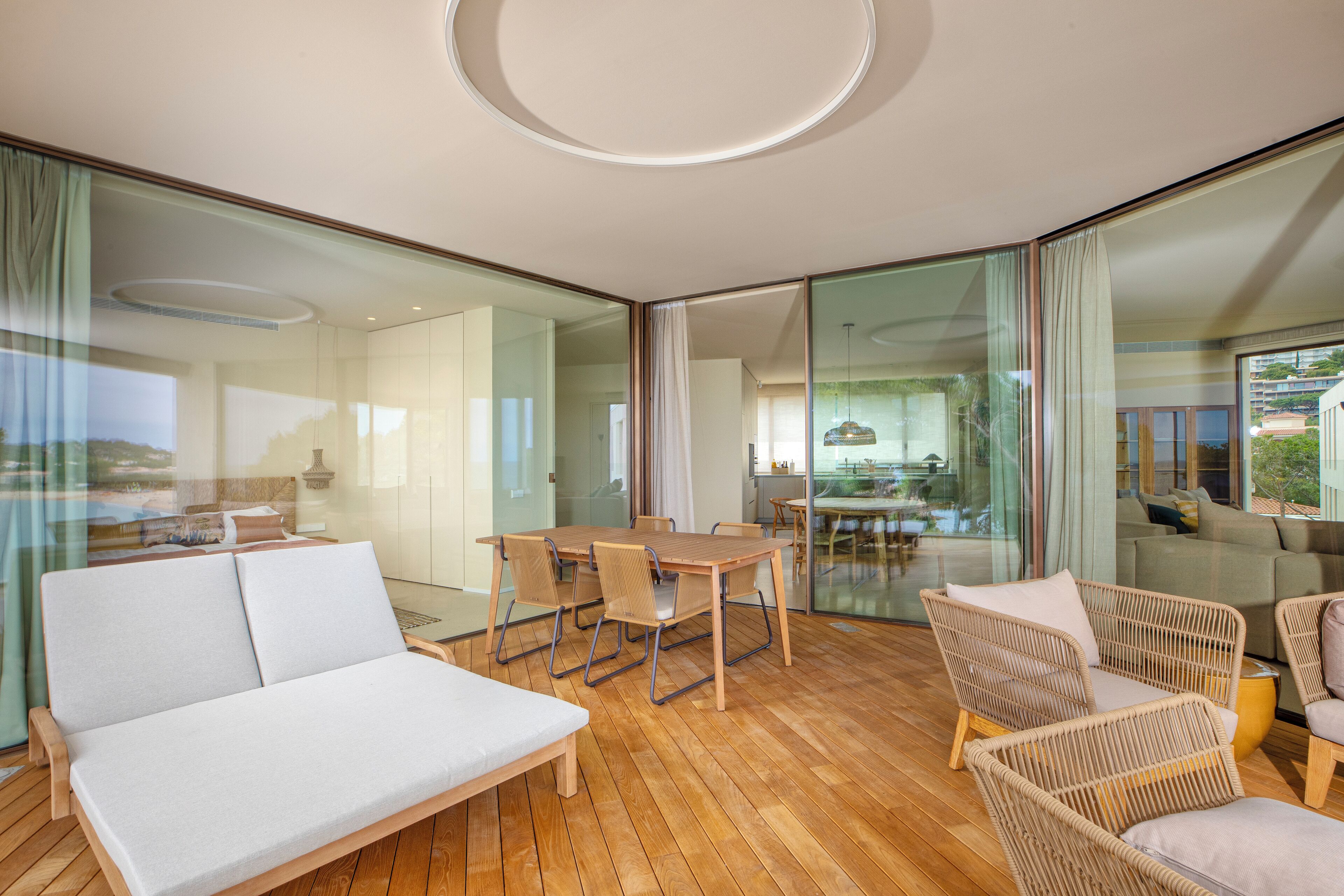 Un interior moderno con piso de madera, un sofá blanco, sillas de mimbre y un separador de vidrio.
