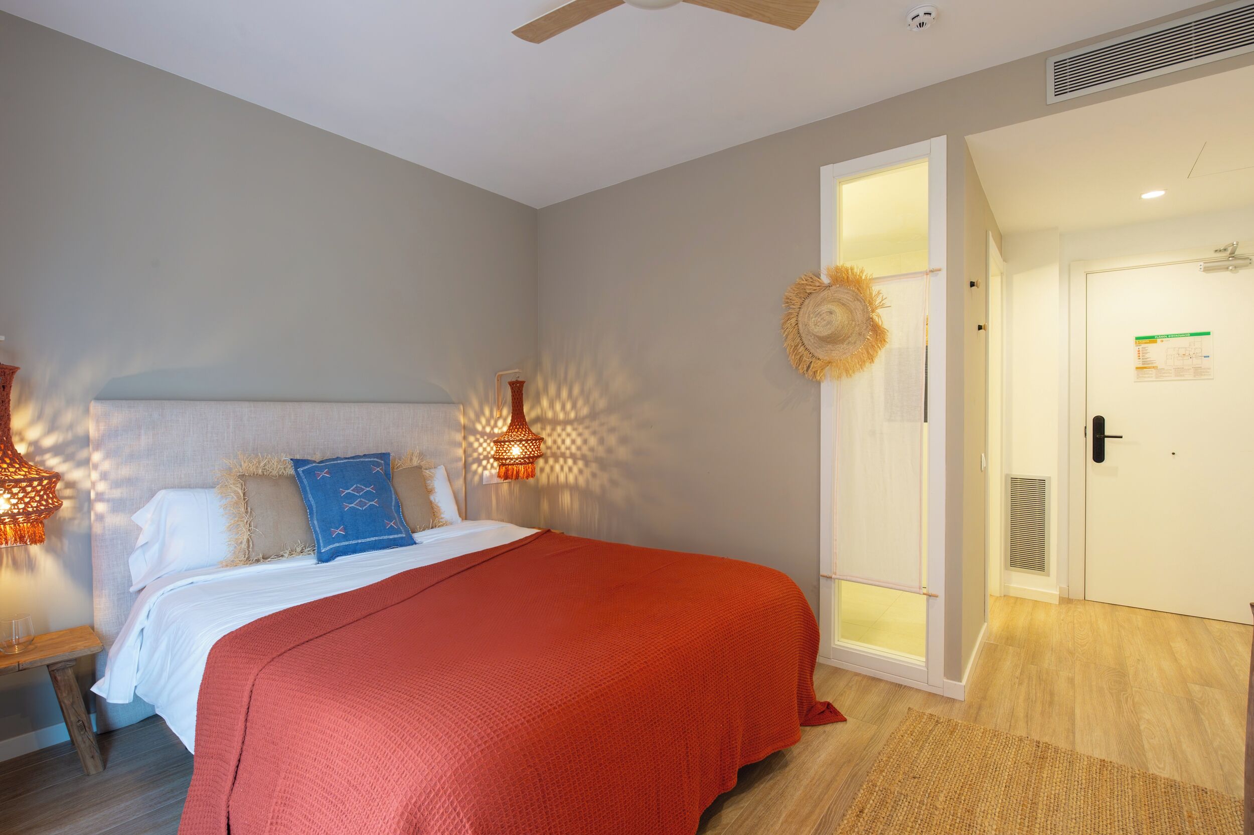 A bedroom with a bed, a nightstand, a wall-mounted lamp, and a door leading to another room.