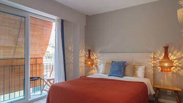 Relax in this serene hotel room featuring a large bed, wall-mounted lamps, and a balcony with a view.