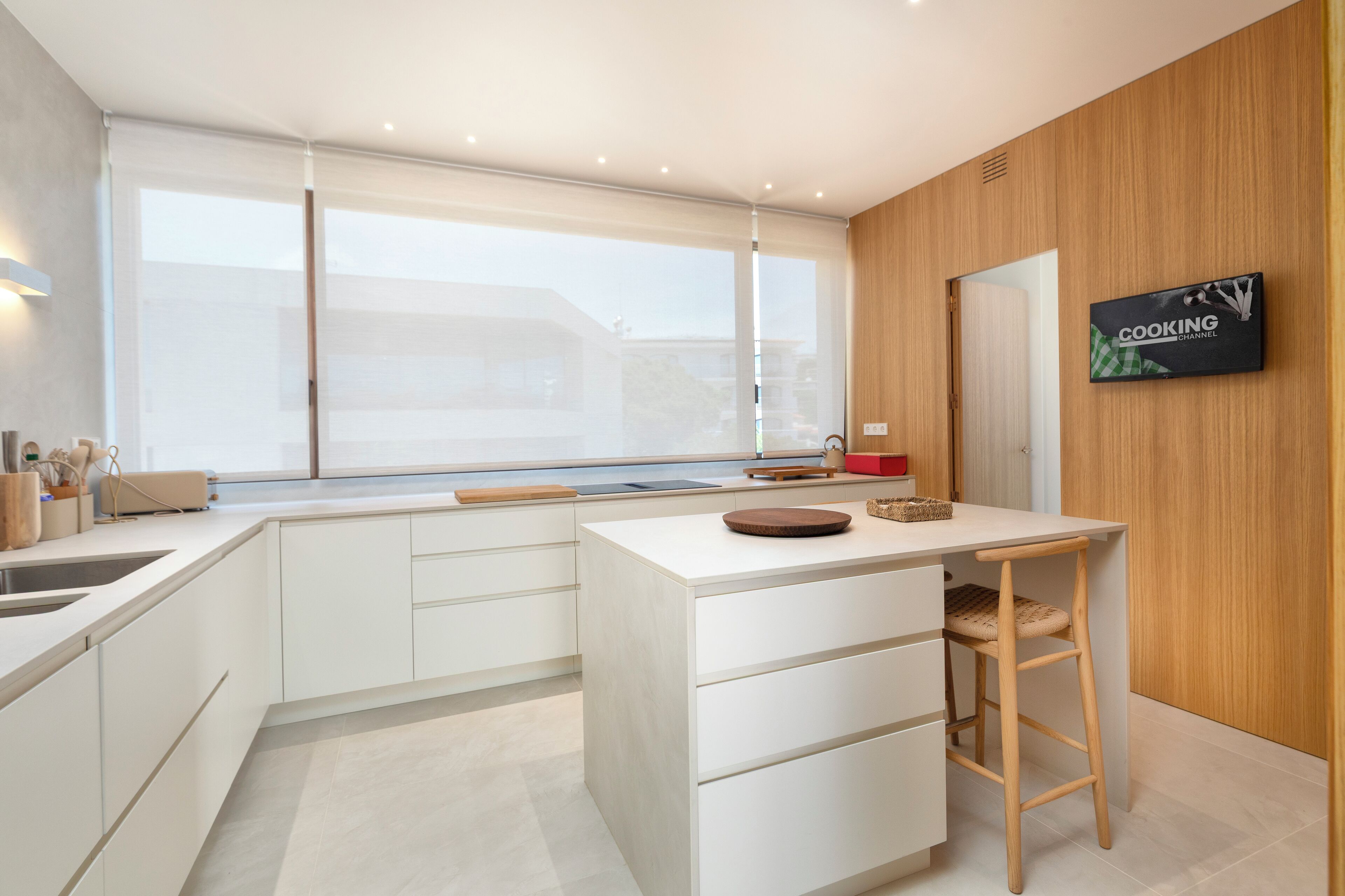A modern kitchen with white cabinetry, a wooden countertop, a large window, and a sign on the wall.