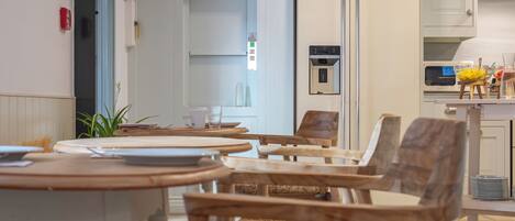 A dining area with round tables and wooden chairs, a white refrigerator, and a kitchen area with a microwave and a small island.