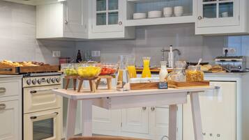 A kitchen with white cabinets, a wooden table with breakfast items, a vintage oven, and a small refrigerator.