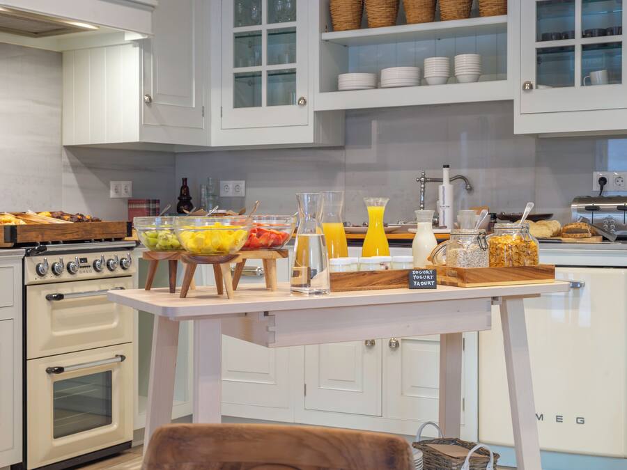 A kitchen with white cabinets, a wooden table with breakfast items, a vintage oven, and a small refrigerator.