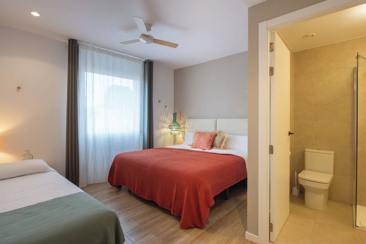 Hotelkamer met een bed, nachtkastje, gordijnen, plafondventilator en een badkamer met douche en toilet.