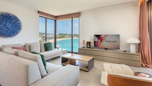 Een moderne woonkamer met een grote televisie, comfortabele zitplaatsen, een bijzettafeltje en uitzicht op het strand.