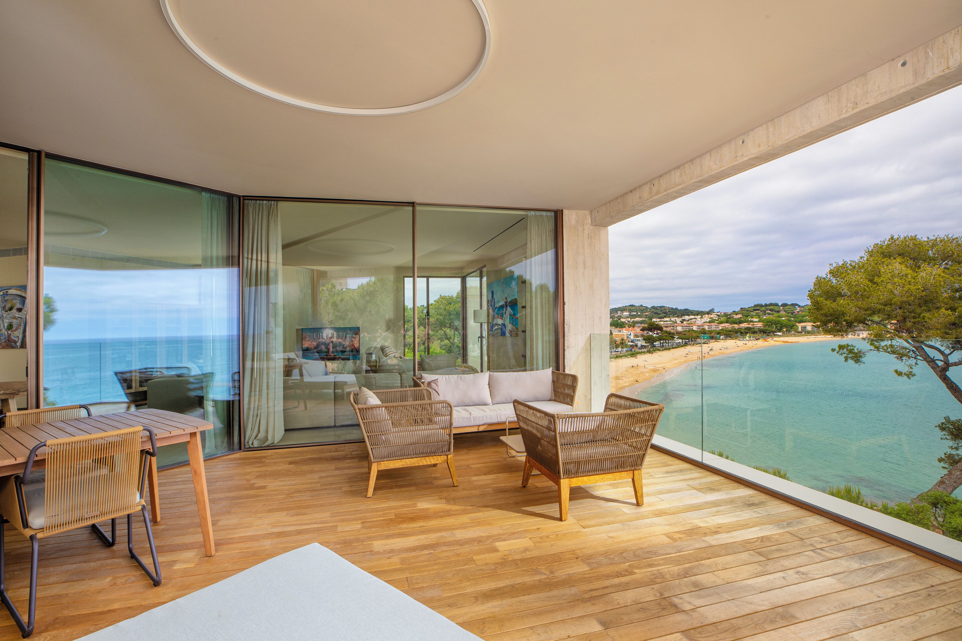 A balcony with wooden flooring, wicker furniture, and a glass door leading to a room.