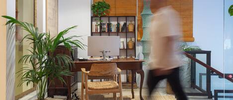 Un interior moderno con un escritorio de madera, una computadora, una estantería y una planta grande en maceta.