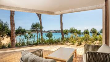 Una terraza de madera con mobiliario de mimbre, con vista a una playa y al mar.