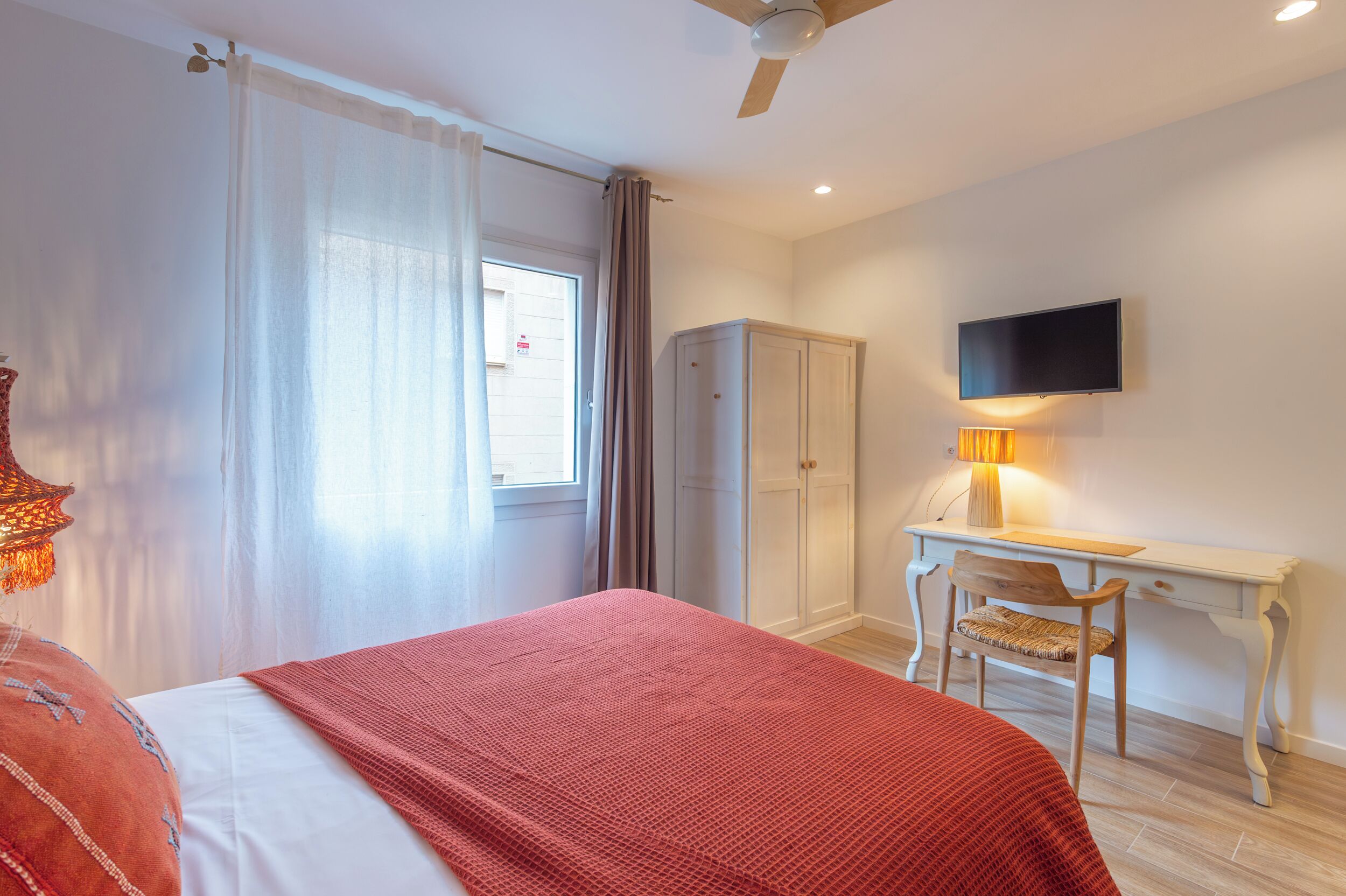 A bedroom with a bed, a desk, a chair, a wardrobe, and a TV.