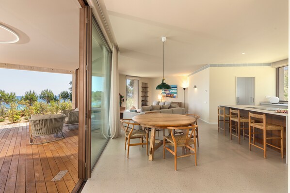 A modern kitchen with a dining area, a large wooden table, and a bar with high stools.