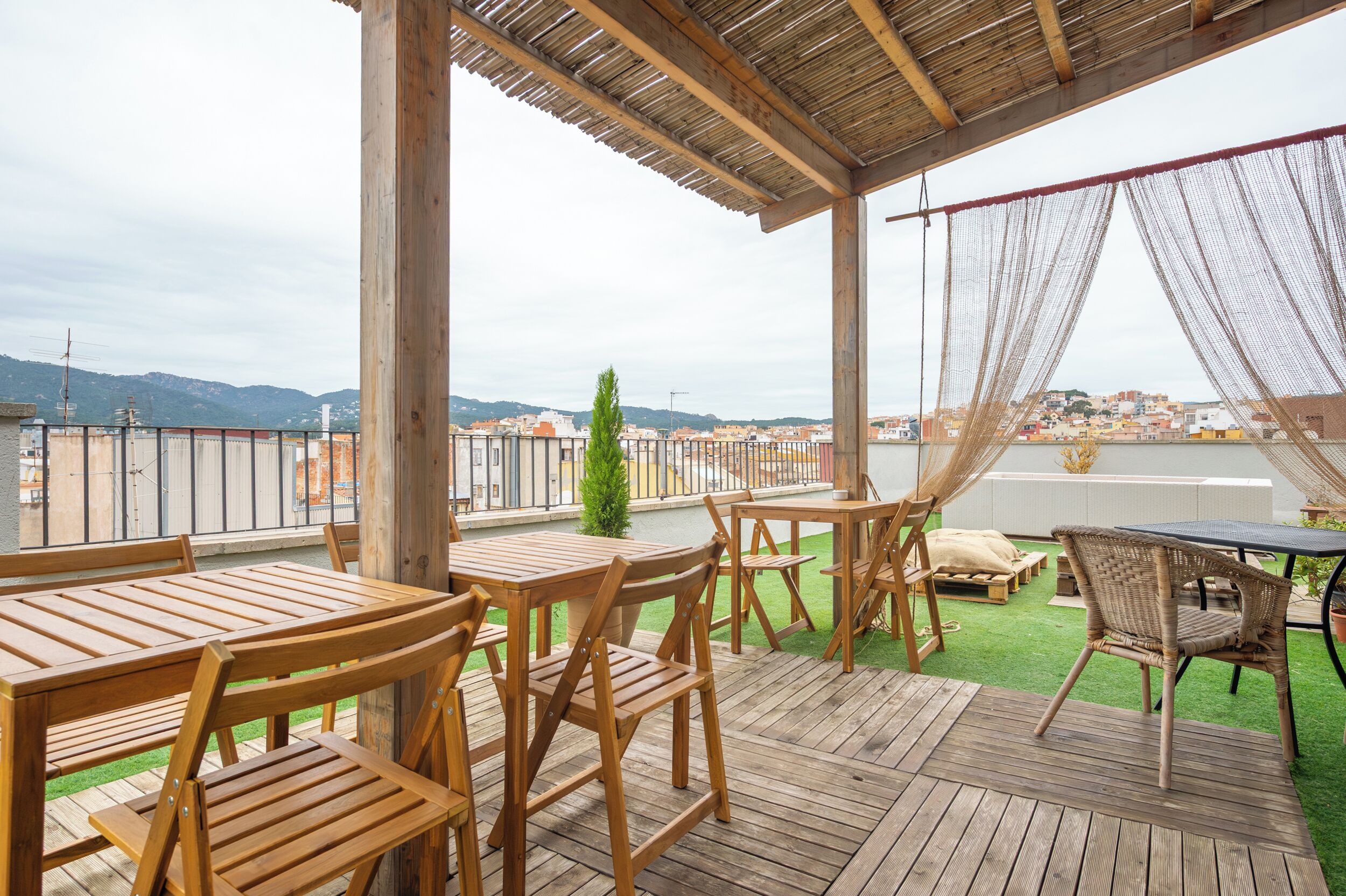Una terraza de madera con mobiliario exterior, una pérgola y vistas a un paisaje urbano.