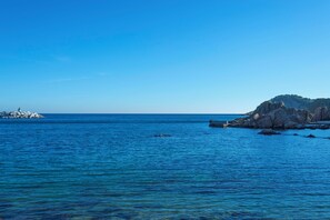 Cena costeira com águas azul-claras, formações rochosas e uma ilha ao longe.