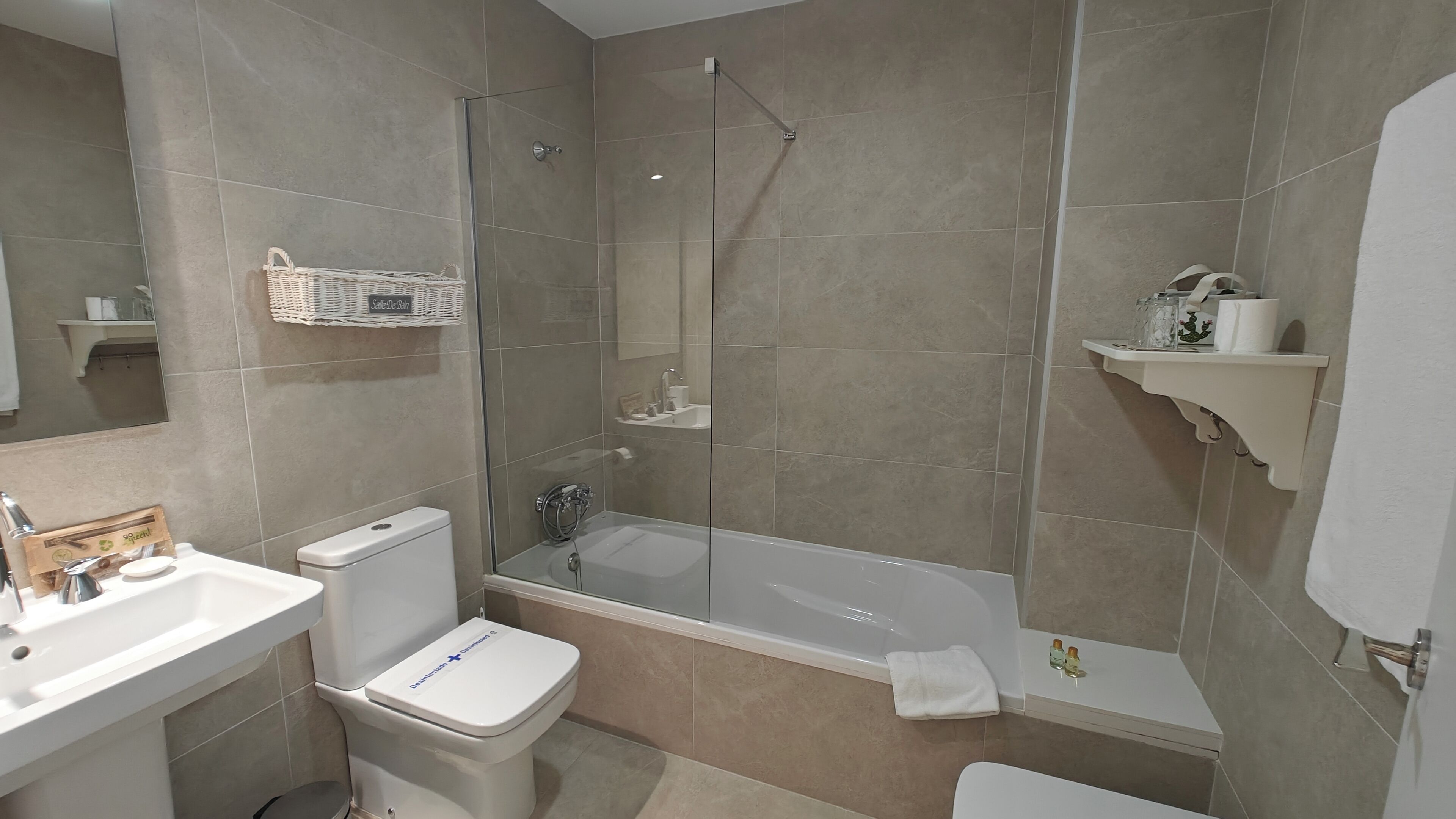 Un baño con inodoro, lavabo y bañera. Hay una zona de ducha con puerta de cristal.