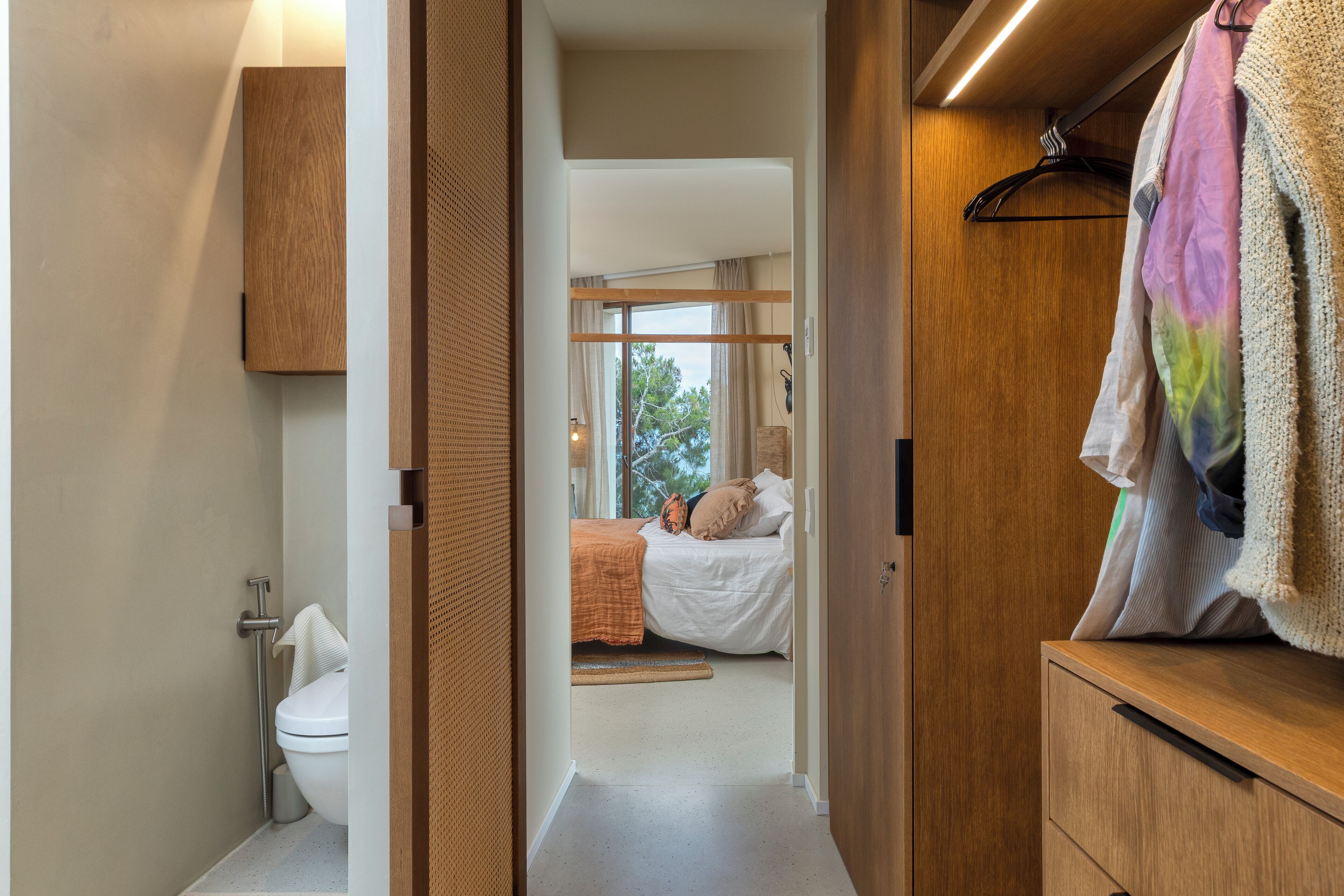 Un pasillo que conduce a un dormitorio con cama, armario de madera y un baño con inodoro y ducha.