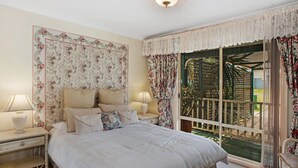 Un dormitorio con una cama grande, dos mesitas de noche con lámparas, papel tapiz floral y vistas a través de una ventana con cortinas.