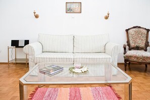 A living room with a striped sofa, a glass coffee table, a floral armchair, and a television on a stand.