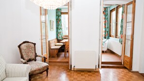 A room with a wooden floor, a floral armchair, a striped sofa, and a dining area with a bench and table. - Marthas Veranda Apartment (Vienna)