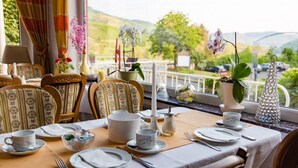A dining table set with white plates, cups, and cutlery, surrounded by chairs with patterned upholstery. - Hotel Weinhaus Moselblick (Burg)