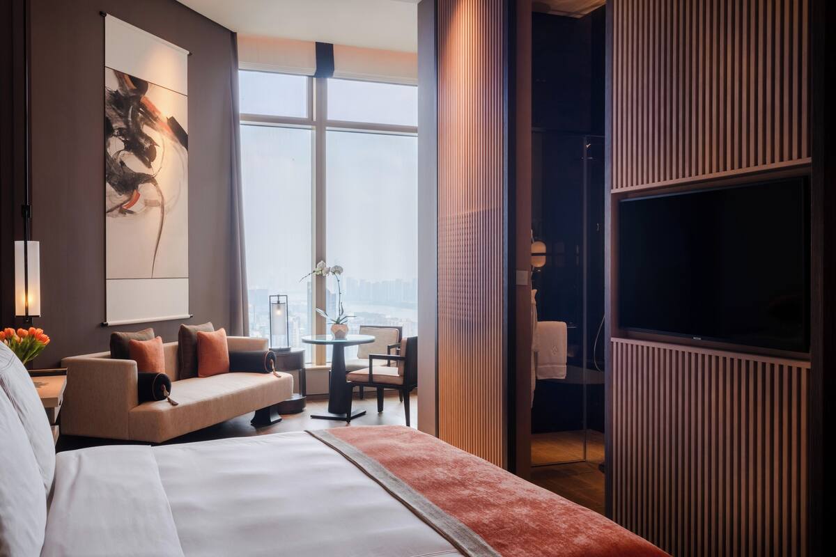 Une chambre d’hôtel avec un lit, un canapé, une télévision et une vue sur la ville.