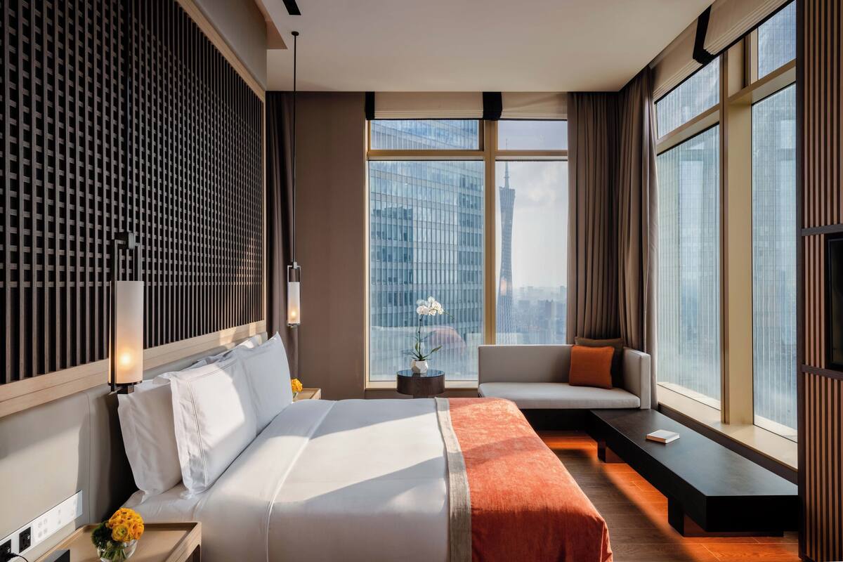 Une chambre d’hôtel moderne dotée d’un grand lit, d’un coin salon près de la fenêtre et offrant une vue sur la ville.