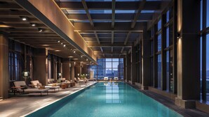 A long indoor swimming pool with lounge chairs and a city view. - Jumeirah Guangzhou (Guangzhou)