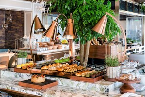 A buffet setup with various pastries and a tree in the background.