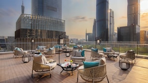 A rooftop terrace with wicker furniture, a coffee table, and a view of modern skyscrapers. - Jumeirah Guangzhou (Guangzhou)
