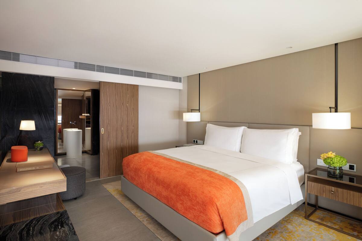 Une chambre d’hôtel moderne, dotée d’un grand lit, de tables de chevet, d’un bureau et d’une salle de bain visible à travers une porte ouverte.