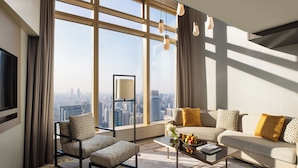A modern living room with a sofa, armchair, coffee table, and a view of a cityscape through large windows. - Jumeirah Guangzhou (Guangzhou)